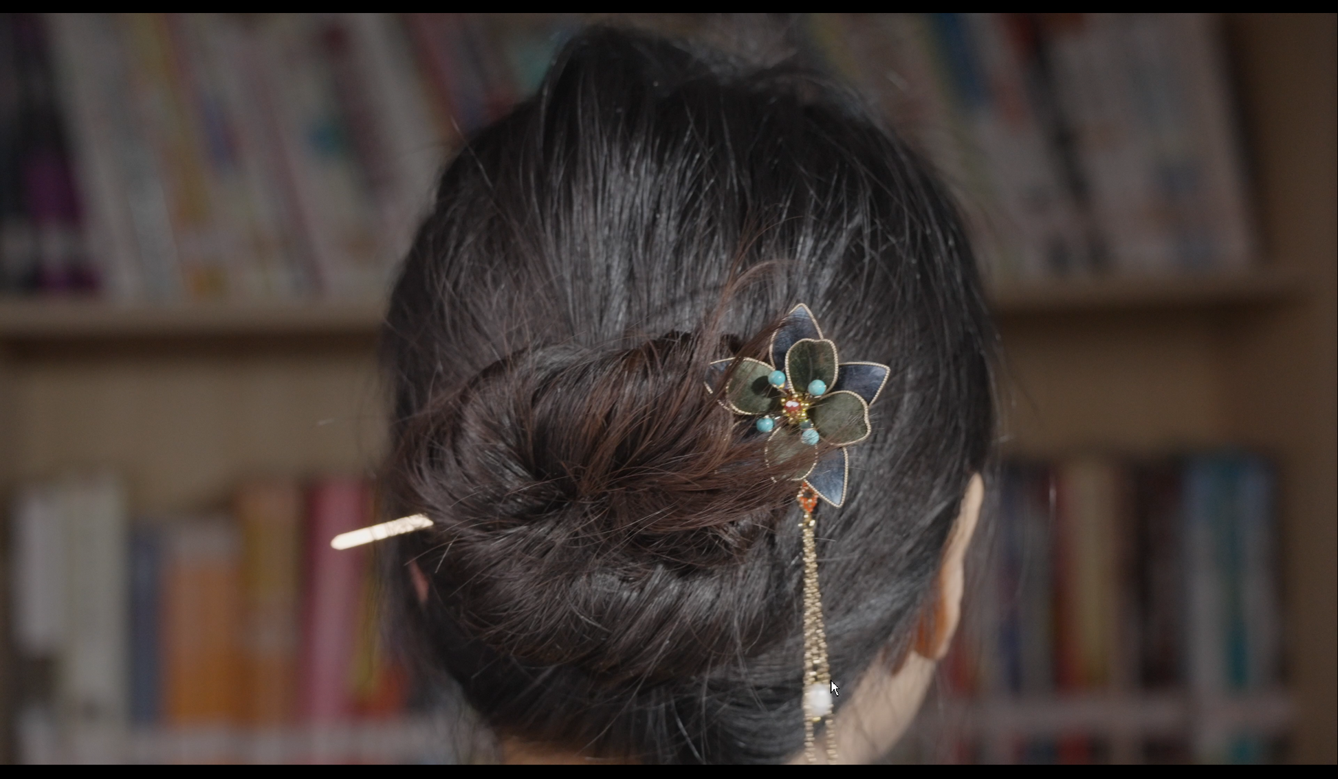 Woman wearing blue-green velvet flower tasseled hair stick in updo hairstyle - styling example