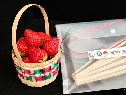 Bamboo lattice basket filled with fresh strawberries next to materials kit with natural bamboo strips on black background