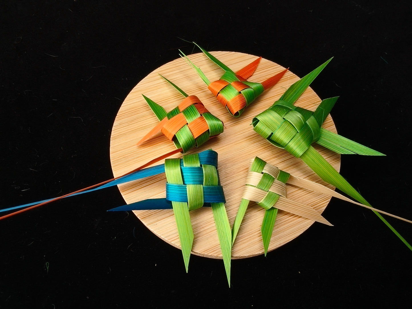 Four bamboo woven tropical fish arranged on round plate with black background - home decor display
