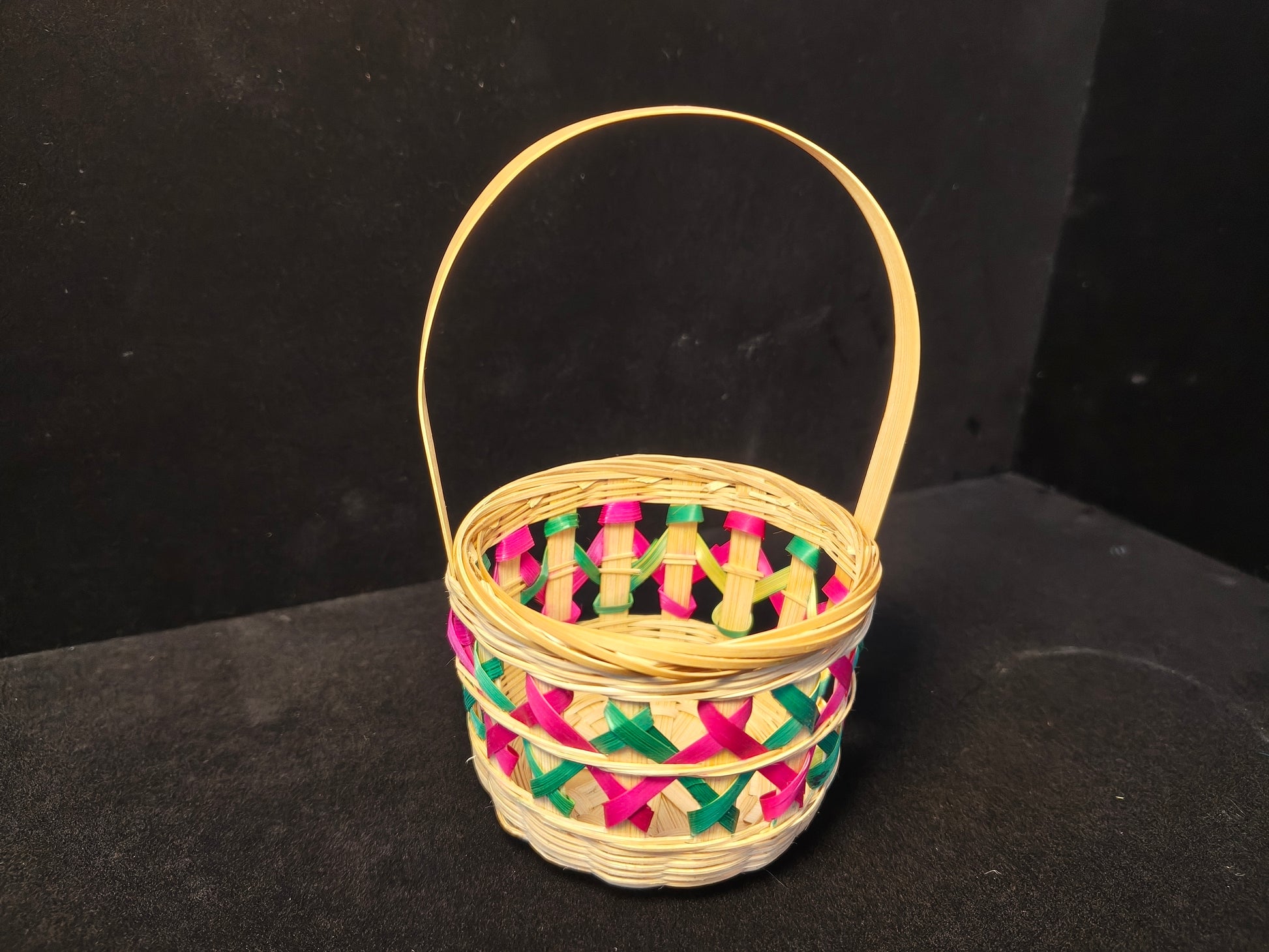 Handmade bamboo weaving basket with colorful lattice pattern and handle on black background - angle view