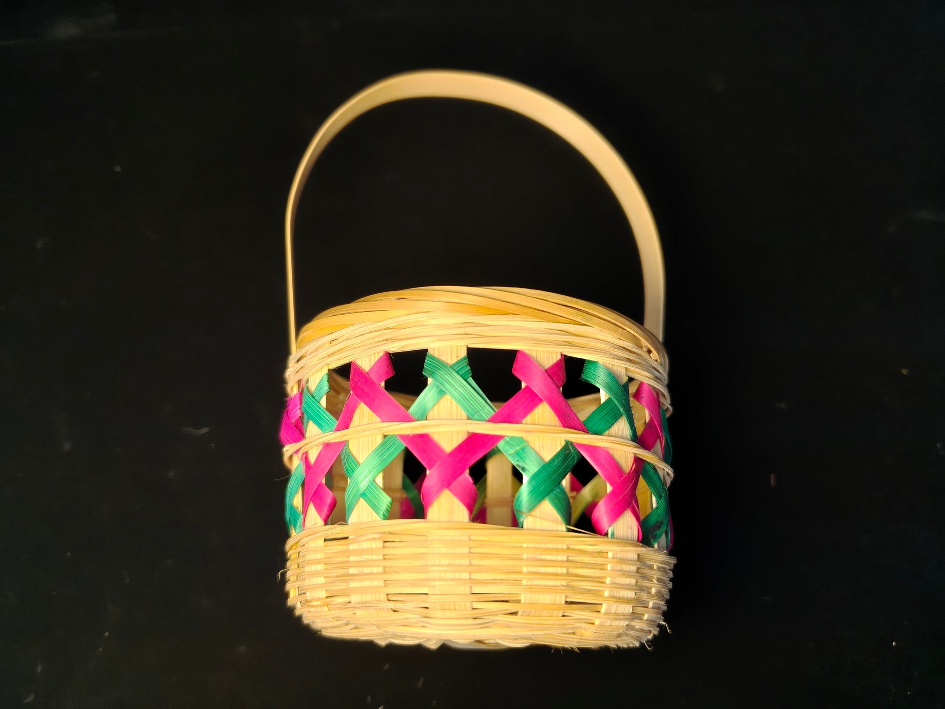 Chinese bamboo woven basket with pink and green lattice design and natural handle on black background - side view