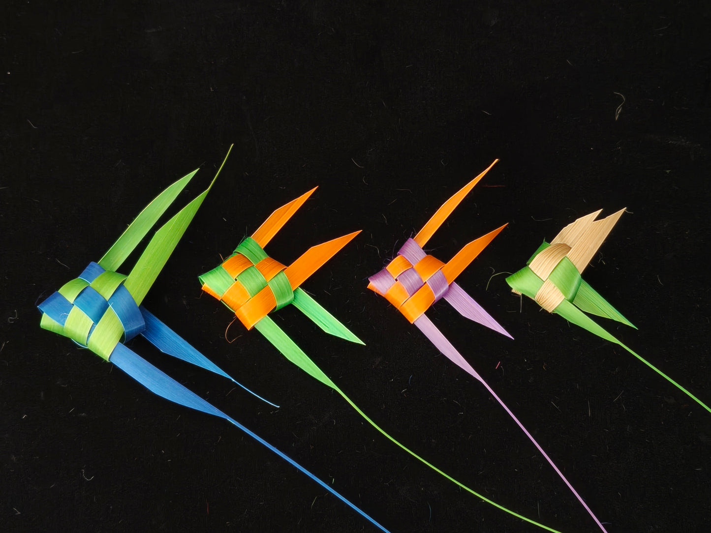 Four colorful Chinese bamboo woven tropical fish in blue, green, orange and pink on black background