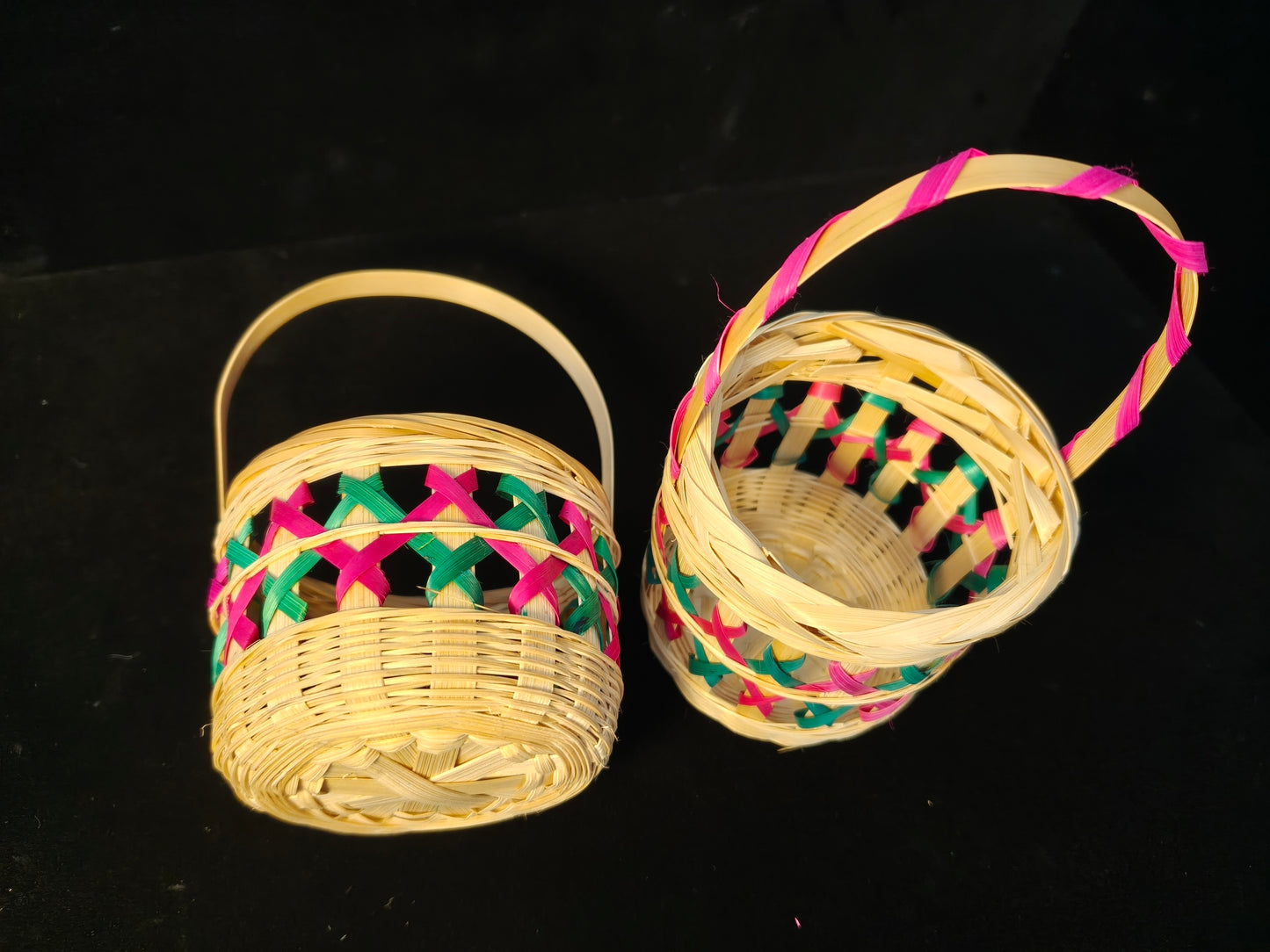 Two identical Chinese bamboo woven baskets with colorful lattice patterns in pink and green on black background