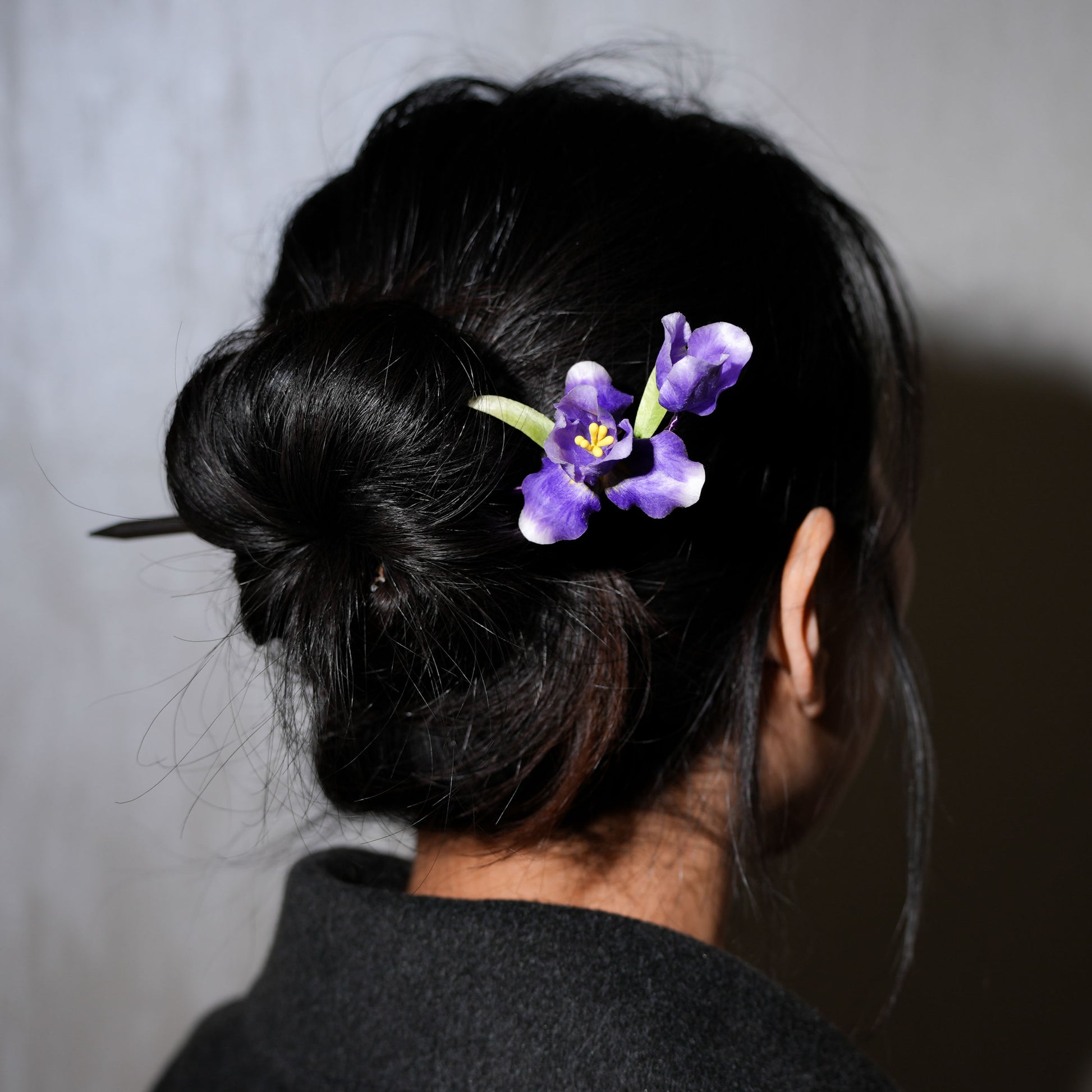 Woman wearing purple iris velvet flower hair stick in updo hairstyle - elegant styling example