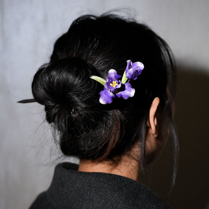 Woman wearing purple iris velvet flower hair stick in updo hairstyle - elegant styling example